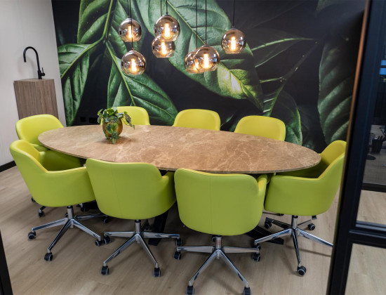 Vergaderruimte met groene stoelen aan een ovale tafel.
