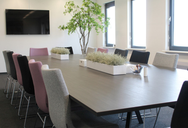 Vergaderruimte met zwarte vergadertafel en gekleurde stoelen.