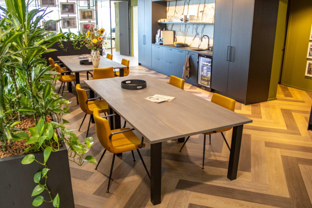 Kantine-inrichting met planten, geel gestoffeerde stoelen en een moderne keuken.