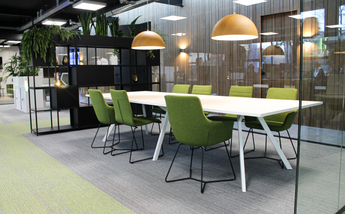 Moderne kantoorinrichting, vergadertafel met groene stoelen en planten.
