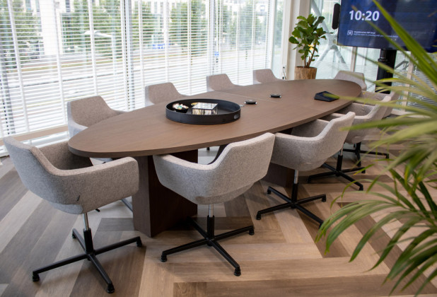 Moderne vergaderruimte met grijs gestoffeerde stoelen aan een ovale vergadertafel.